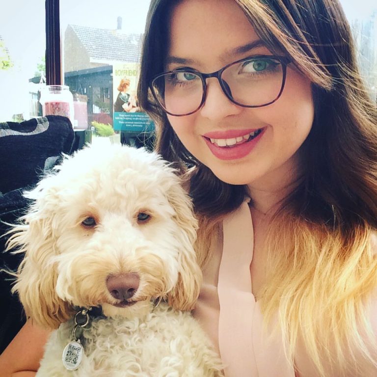 Celebrating National Dog Day, Jenni with her arm around a white, curly haired dog with brown eyes and a brown nose