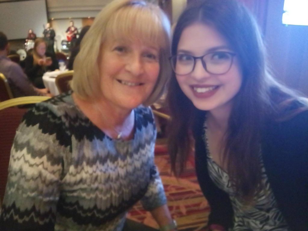 Jenni smiling at the camera, wearing glasses. On her left is a woman with blonde hair, also smiling.