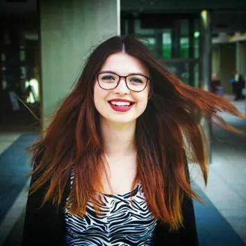 A close up of Jenni smiling. Her hair blowing away from her. She is wearing a black and white top.