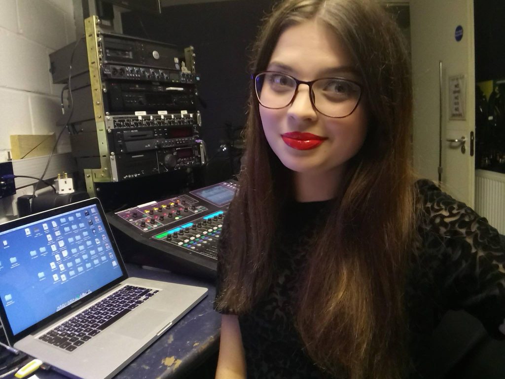 Jenni with long brown hair and red lipstick, sat in front of her laptop.