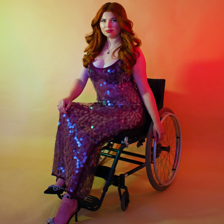 Celebrating Disability Pride, Jenni sat in her manual wheelchair wearing a purple sequin dress looking powerful