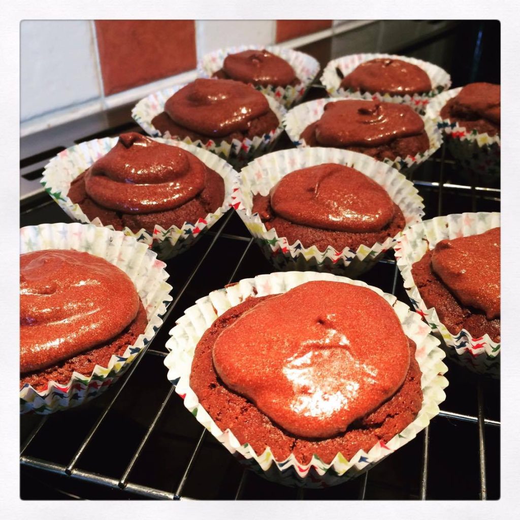 Various baked cakes in cases, with chocolate icing on top.