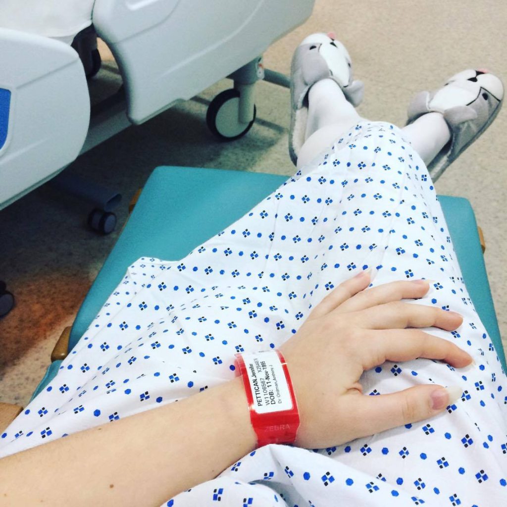 A POV photo of Jenni in a hospital gown. She is wearing dog slippers, and has a hospital band in view.