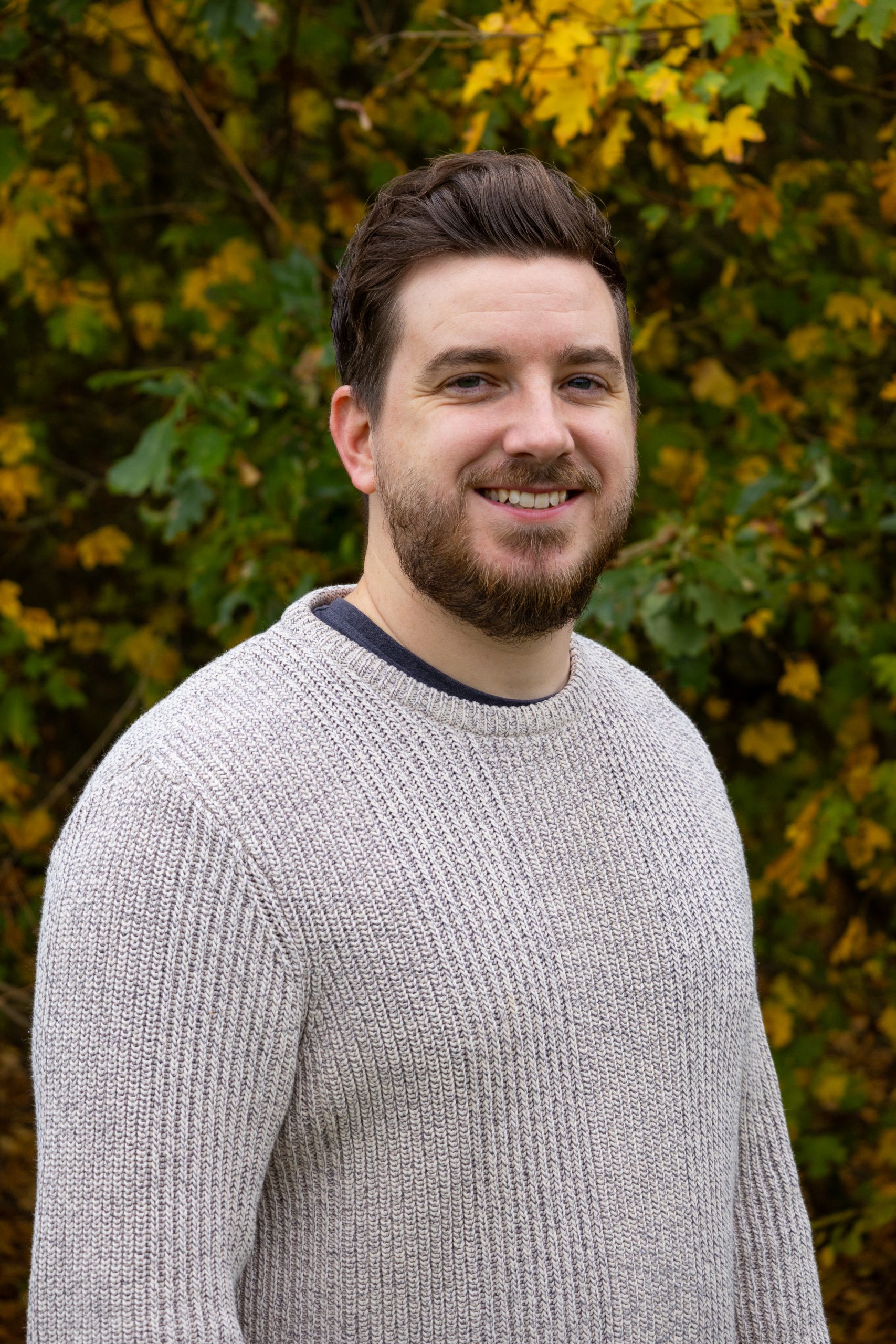 Ian, a male with brown hair and a beard, looking slightly sideways at the camera, wearing a grey knit jumper.