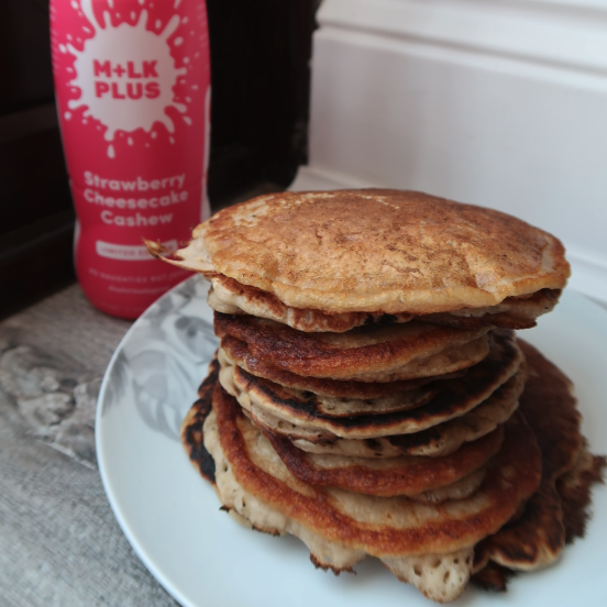 A pile of pancakes with cream in a bottle in the background.