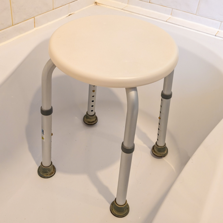 A shower stool, resting in a bath with a gran rail nearby