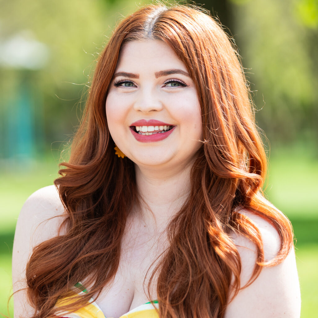 a Headshot of Jenni smiling with her hair in loose curls and her makeup done