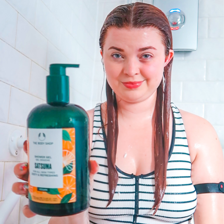 Jenni sitting in the shower wearing swimming costume holding a bottle of shampoo with an easy-pump lid.