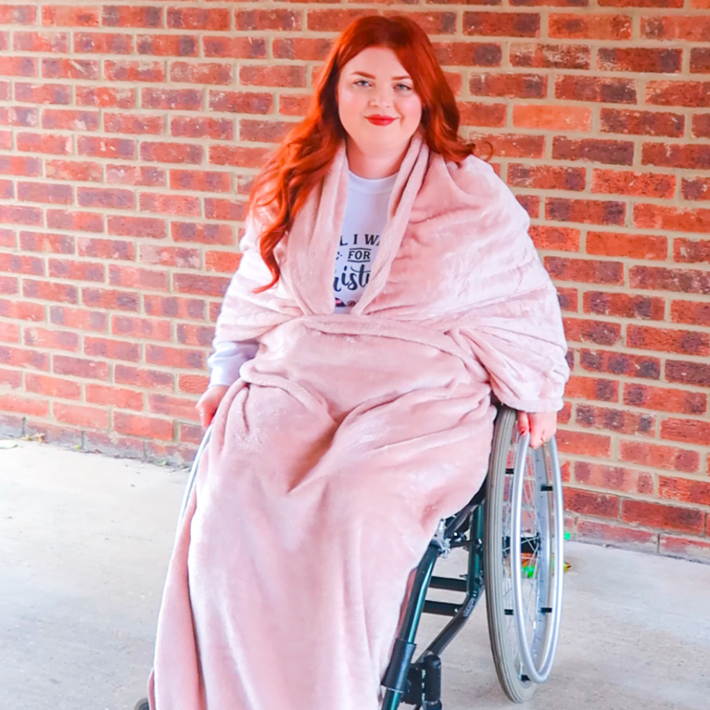 Jenni sitting in a wheelchair, with a pink blanket covering the majority of her.