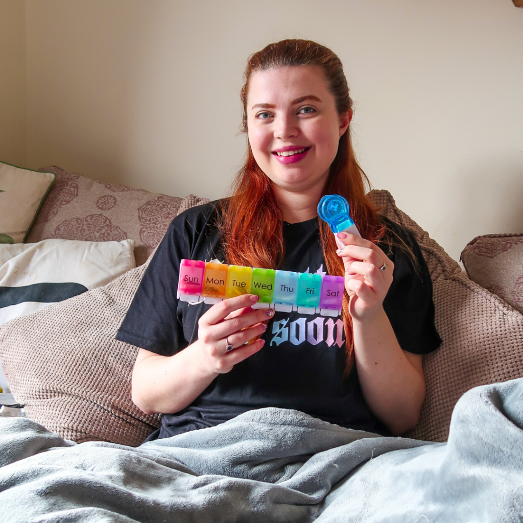 Jenni sitting on a bed, holding her pill popper tool. She is smiling.