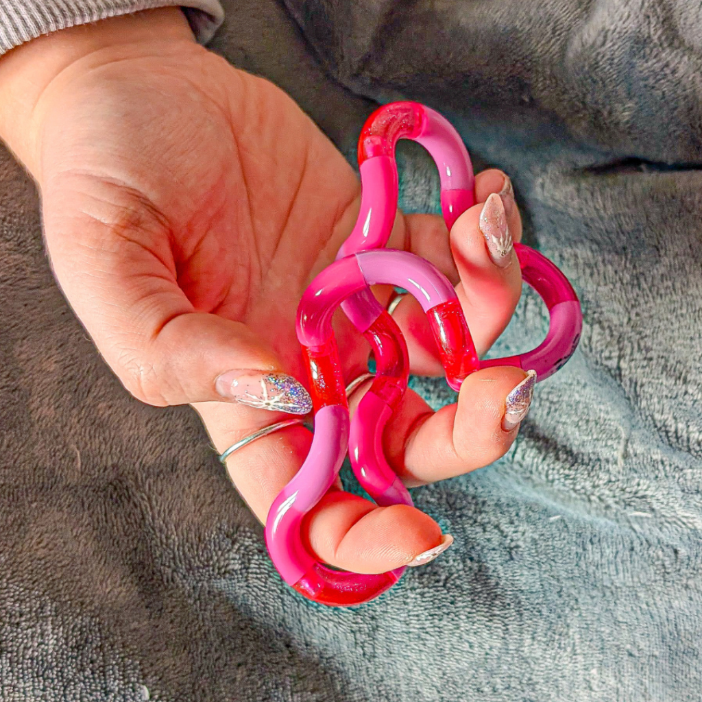 A hand holding a pink tangle fidget toy