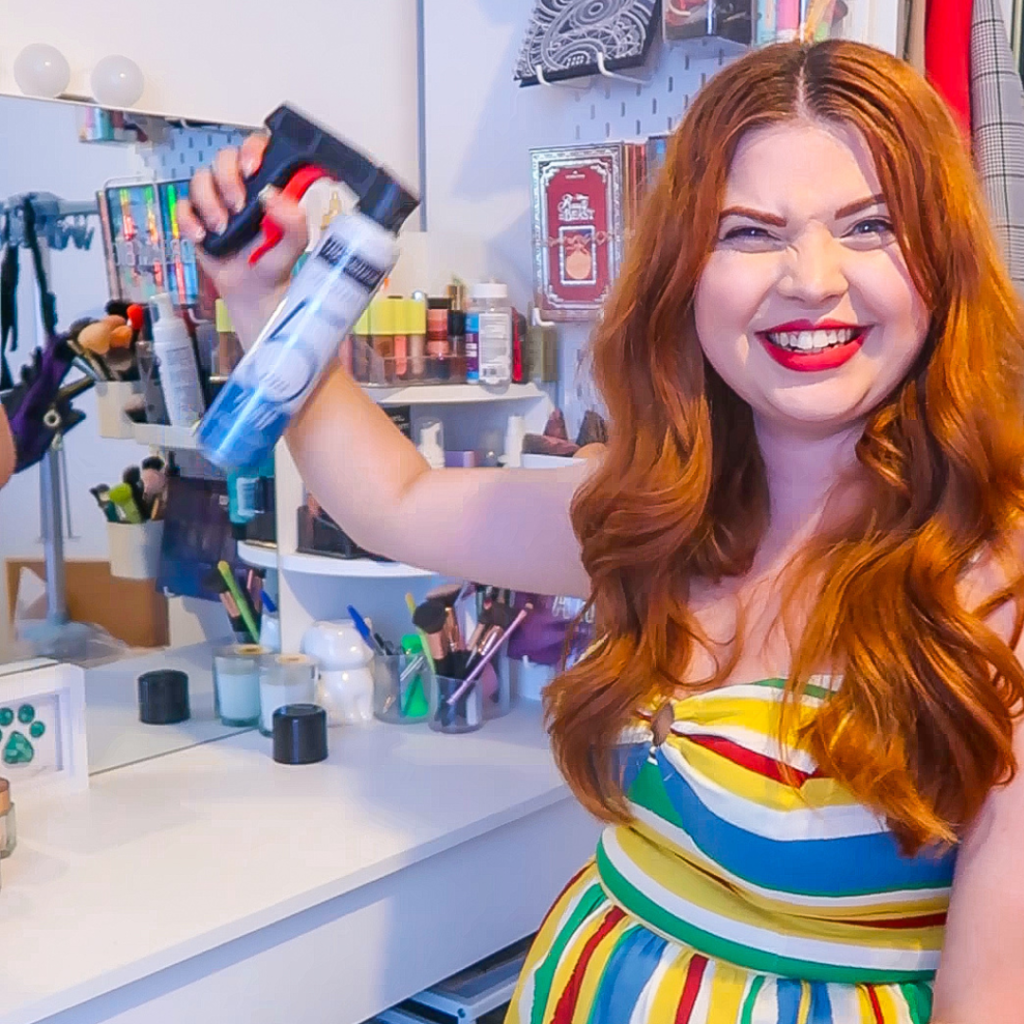 Jenni sitting holding a spray can gun, grinning widely.