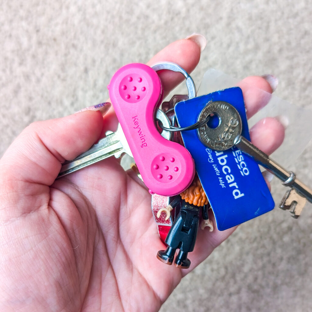 Jenni's hand holding a set of keys. The key has a pink keywing aid on in to make the top of the key larger.