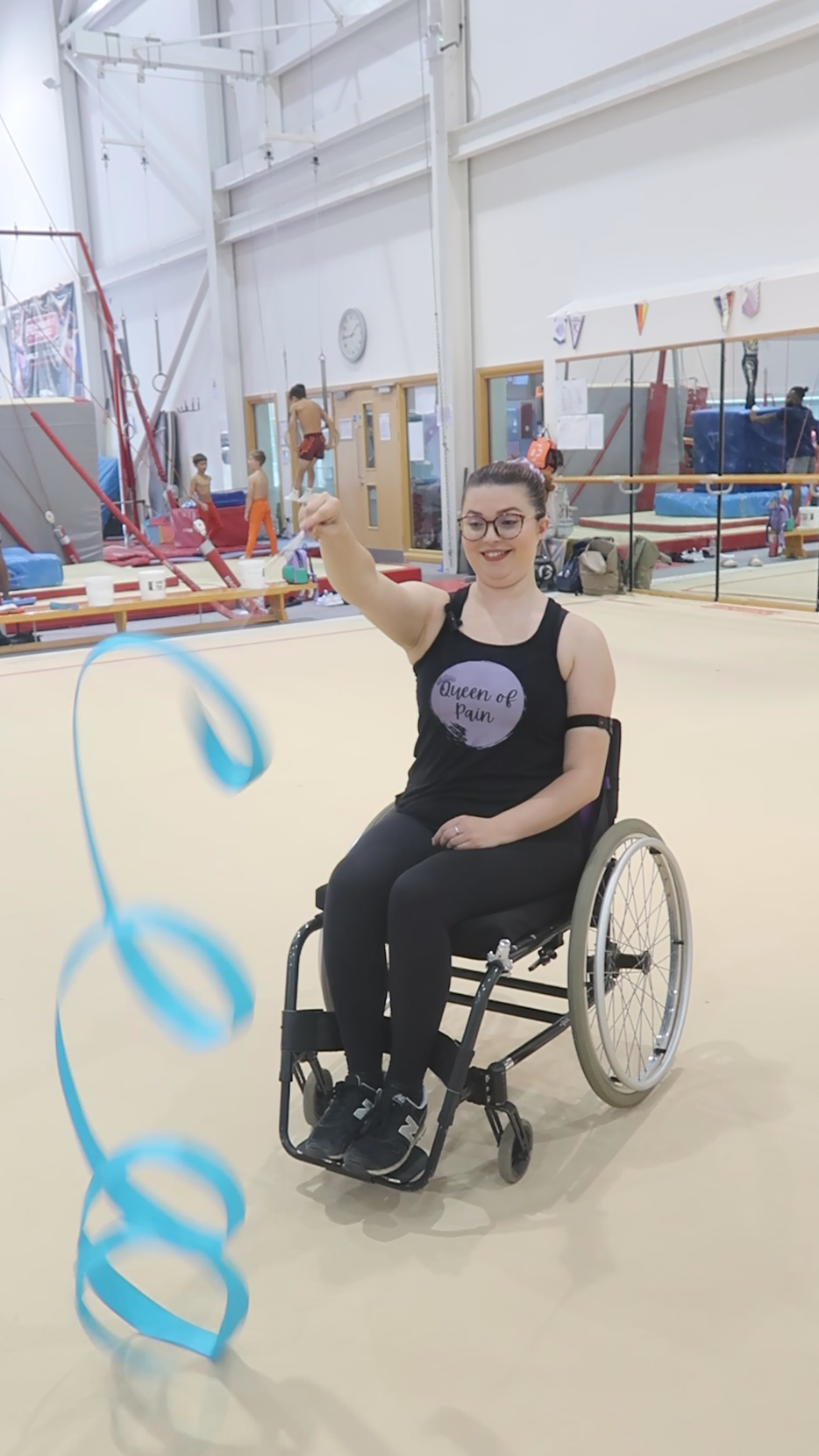 Jenni sat in her manual wheelchair in a gymnastics centre twirling a blue ribbon in circles in front of her