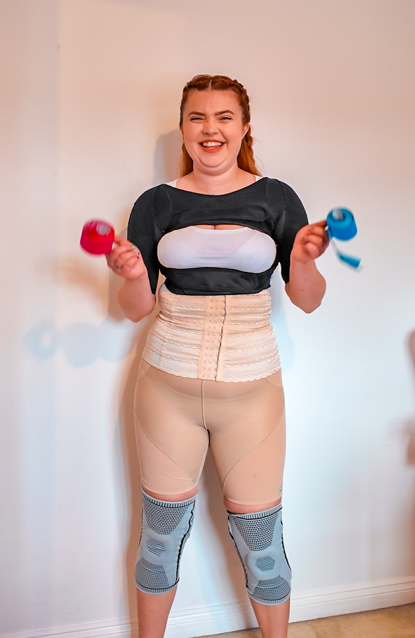 Jenni wearing various support devices across her whole body in different colours, smiling.
