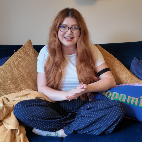 jenni wearing a white t shirt and blue pinstripe trousers on her blue velvet sofa wearing her black visible armband