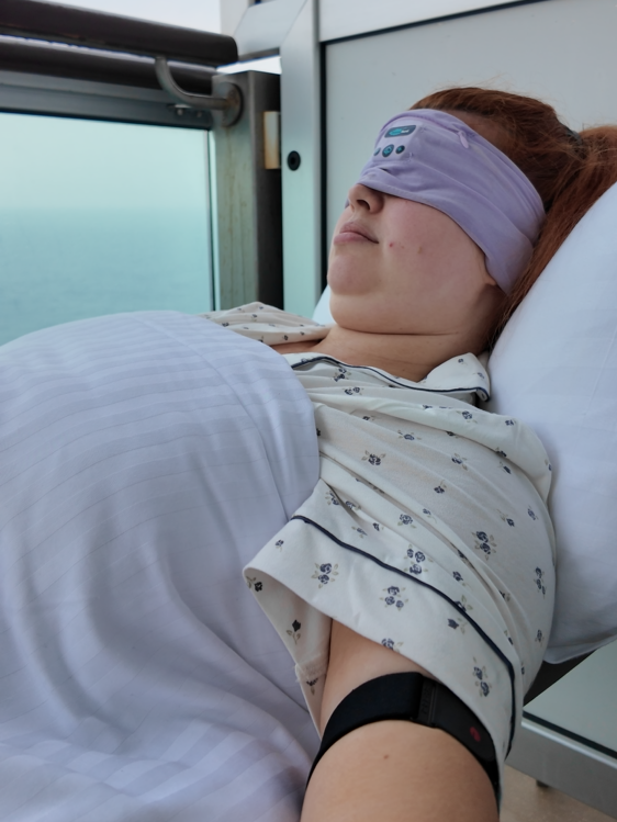 Jenni lying asleep on her cruise ship balcony wearing a eye mask and her visible armband