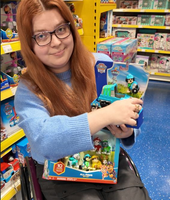 jenni in a toy store holding a Rex toy from paw patrol he is a dog with wheels instead of back legs