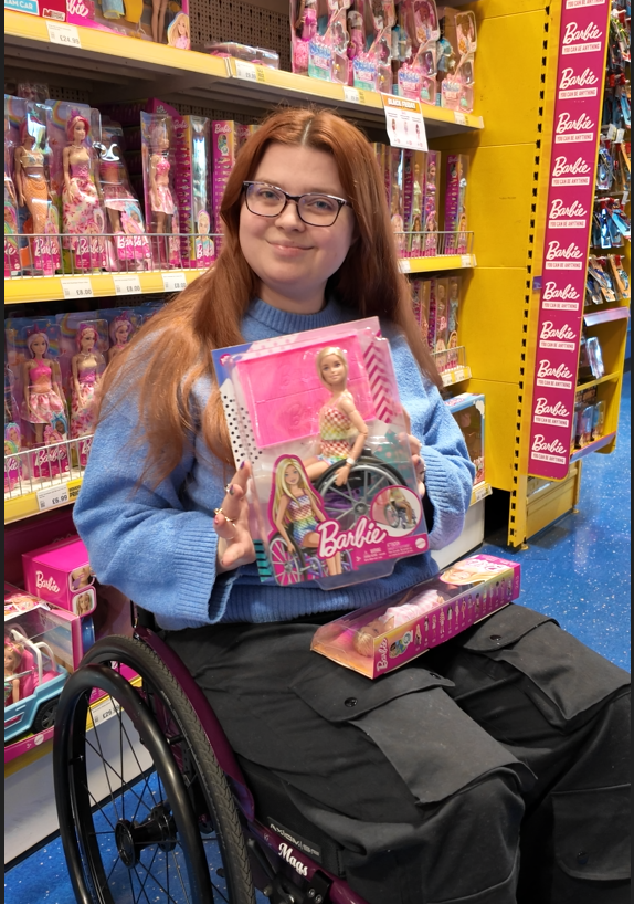 Jenni in the barbie aisle of a toy store holding a wheelchair barbie