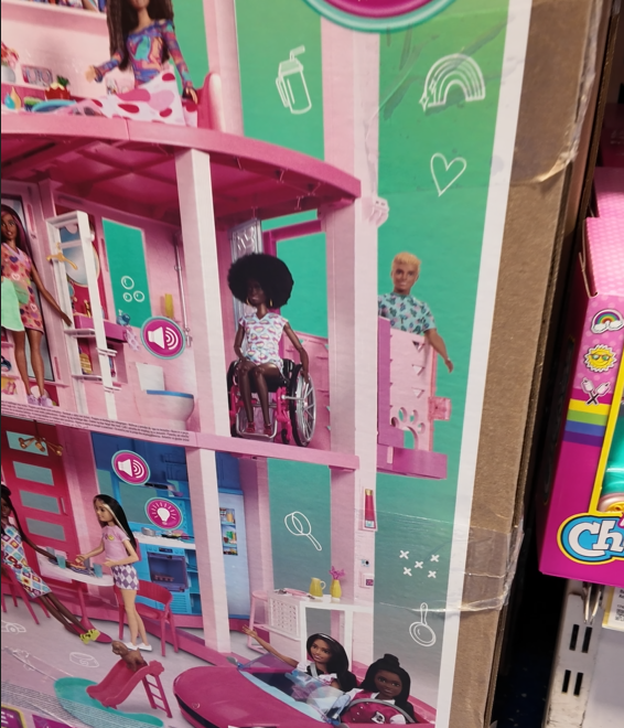 an image of the box of a barbie dream house which has a lift showing a ken doll in the lift and a wheelchair using barbie on the second floor