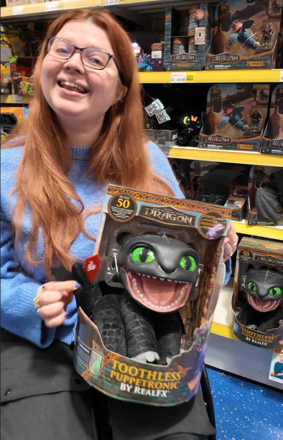 jenni smiling in a toy store holding a toothless toy from how to train your dragon