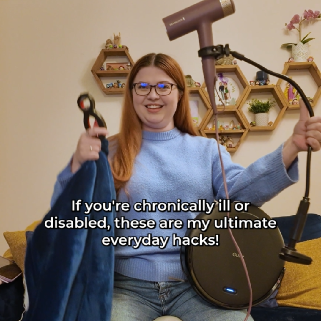 Jenni sitting on a wheelie stool in her living room holding her other ultimate chronic illness hacks including a hairdryer stand, robot vacuum, heated blanket and 6-in-1 multiopener tool