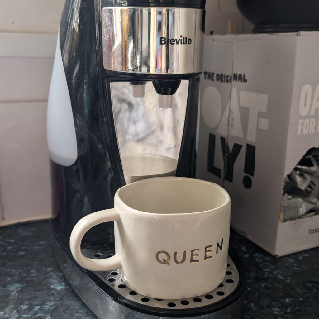 Jenni's one cup breville kettle which is black and silver. instead of a traditional kettle it has a dispenser for the water and a mug sat under that.
