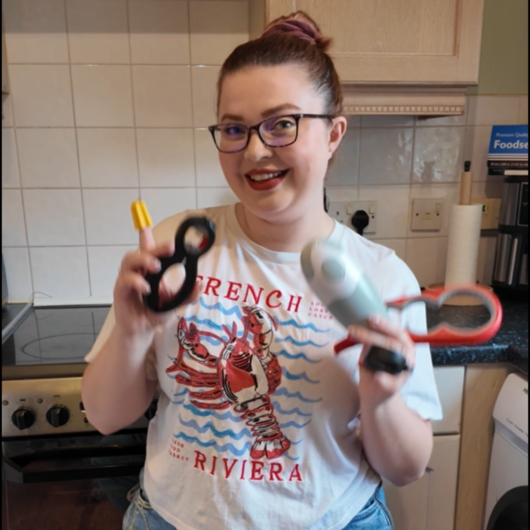 Jenni smiling at the camera holding several jar opener tools including a yellow nimble 1 finger opener, her 6 in 1 opener tool, electric tin opener and bottle and jar opener