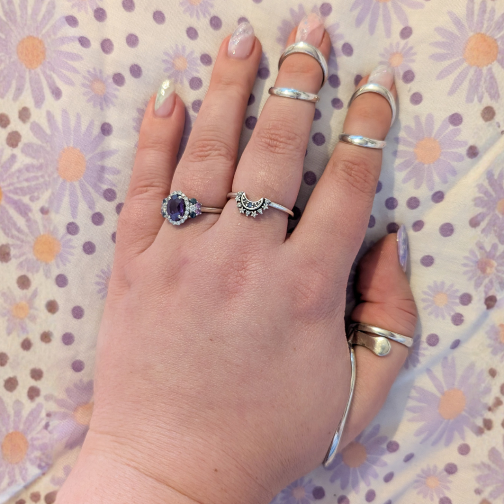 an image of Jenni's hand on a flowerly bedspread wearing 3 silver ring splints, one on her thumb and one on her index and middle fingers
