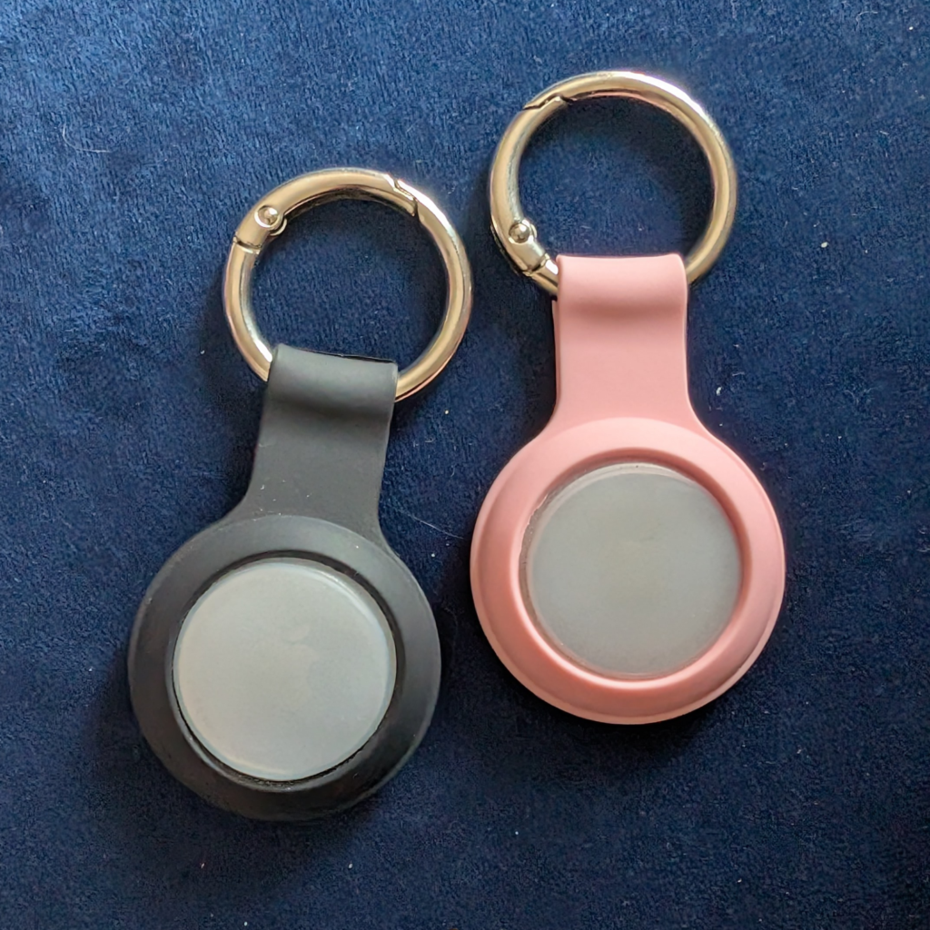 two air tags on pink and black keyring cases 