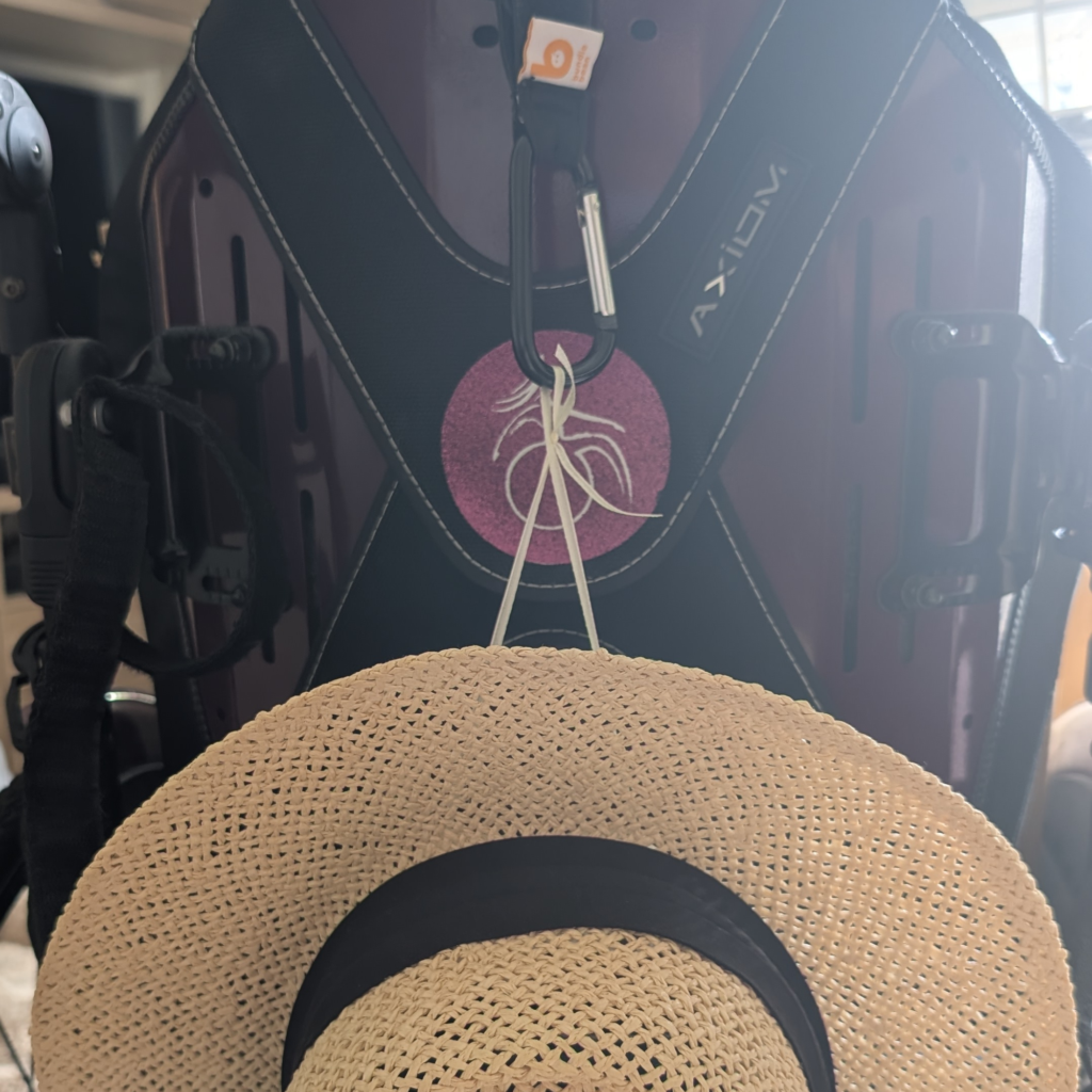 Hat string attached to a carabina on the back of jenni purple wheelchair 