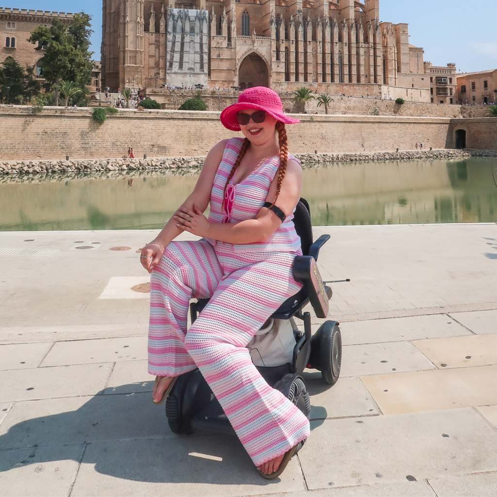 Jenni wearing pink and purple striped matching set in power chair showing her visible black arm band on her left arm 