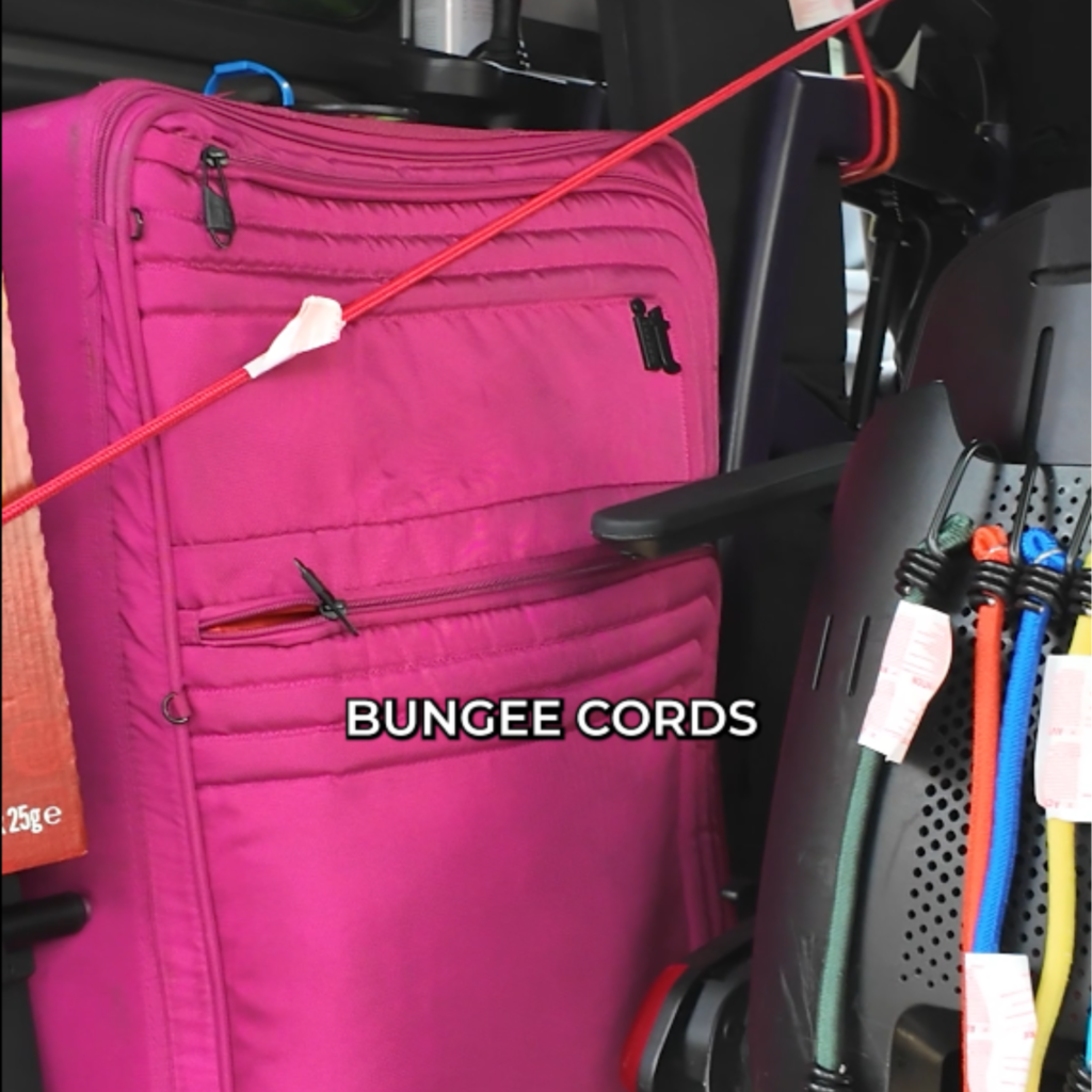 shows pink suitcase  and wheelchair in boot of car secured with bungee cords around them 