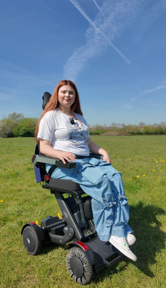 Jenni fully raised up in the XSTO M4 powerchair with her legs dangling unable to reach the footplate